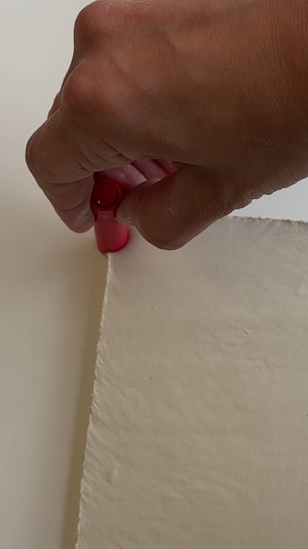 Hand pressing a pen cap into the edge of soft air dry clay to create spiral binder holes for a DIY clay notepad design.