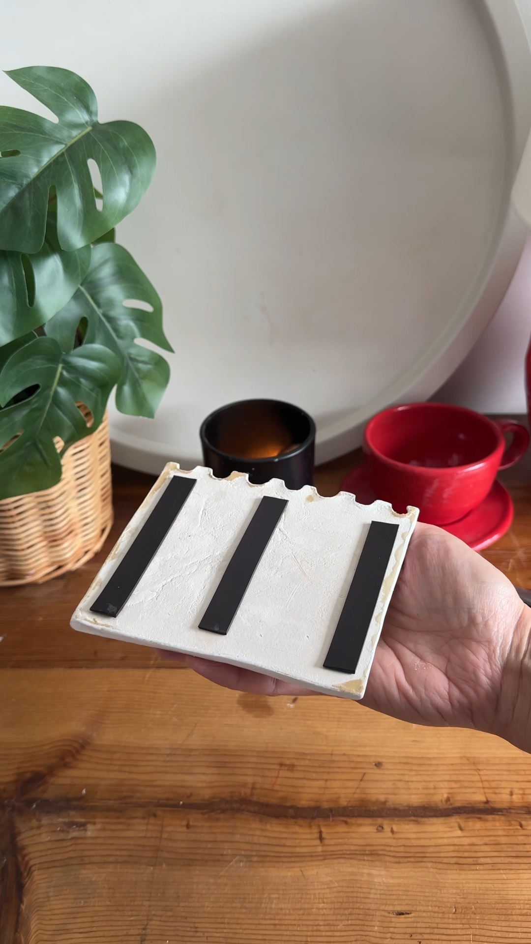 Hand holding the back of a handmade air dry clay notepad magnet with three magnetic strips attached for mounting on a fridge.
