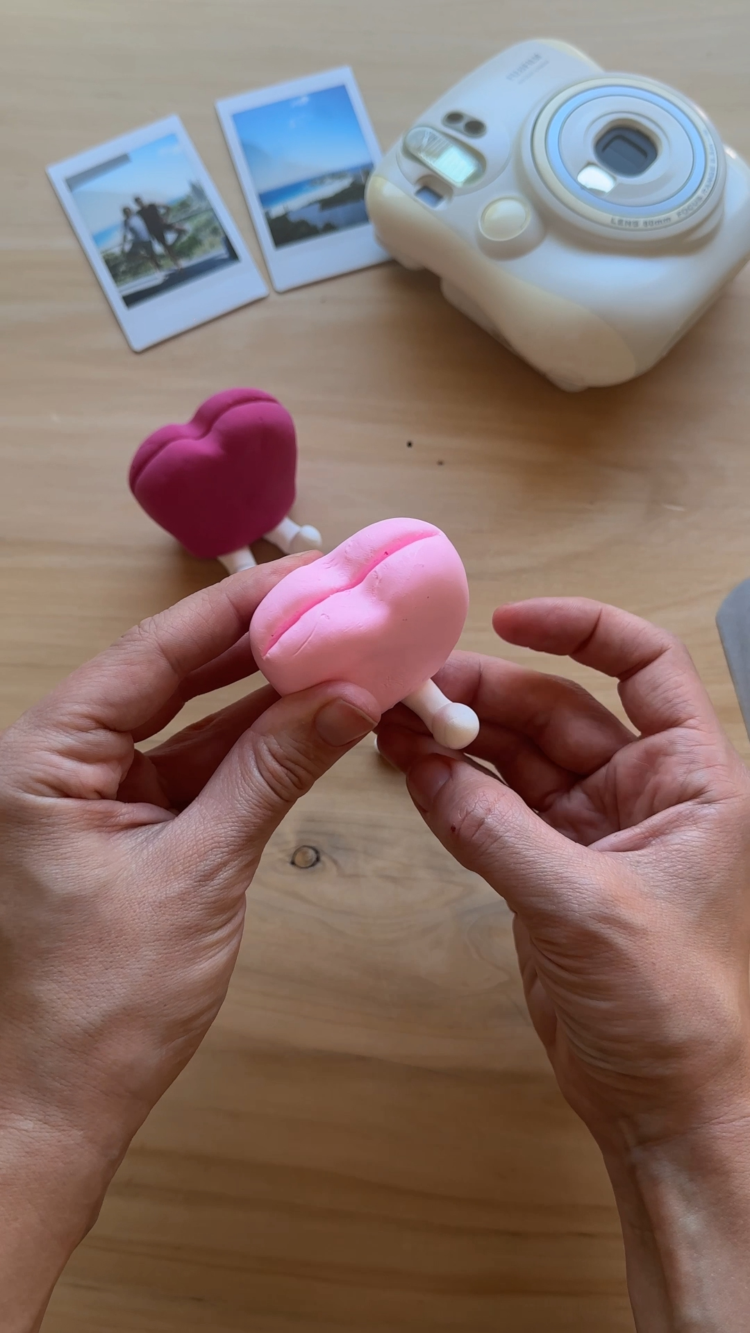 Hands pressing and adjusting the small white foam clay legs on the bottom of a pink heart-shaped foam clay photo holder, stabilising the base so the holder can stand upright on the table.