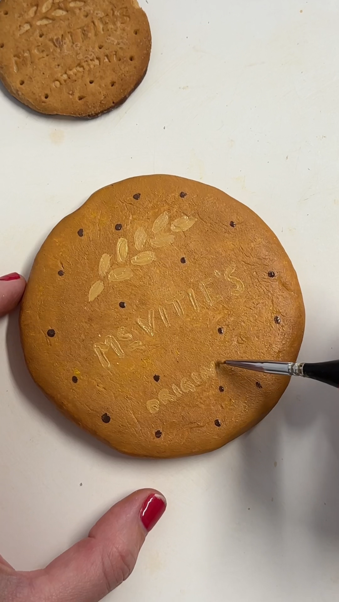 Painting the underside of the clay coaster with warm biscuit-coloured acrylic paint and adding small biscuit texture dots.