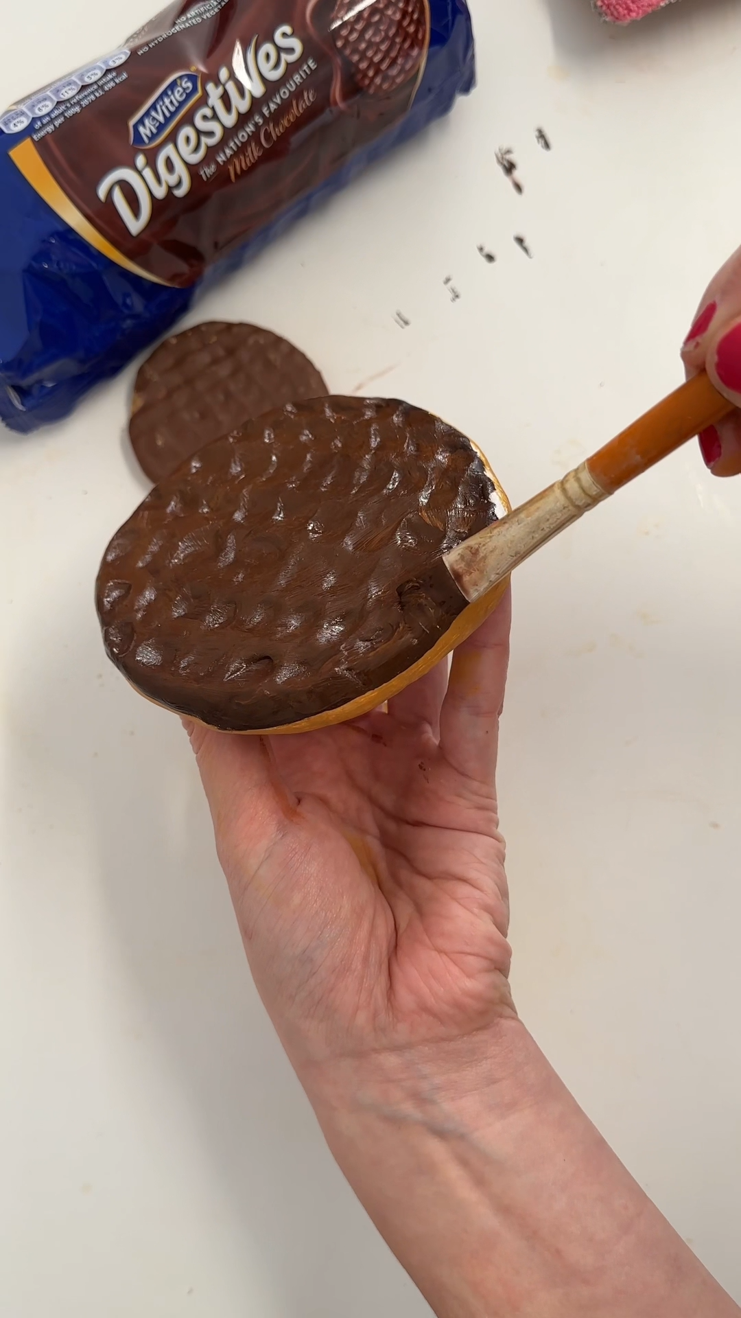 Applying dark chocolate brown paint to the textured top of the clay coaster to create a realistic chocolate digestive effect.