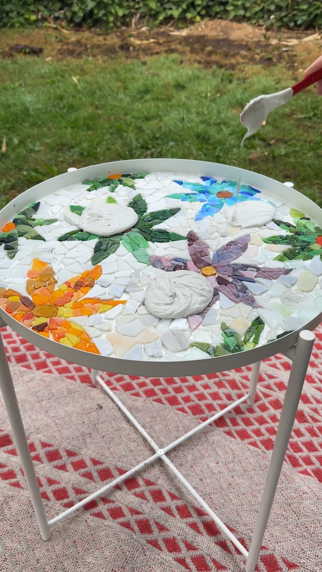 Grout being added onto a colourful floral mosaic tabletop before spreading it across the tiles.