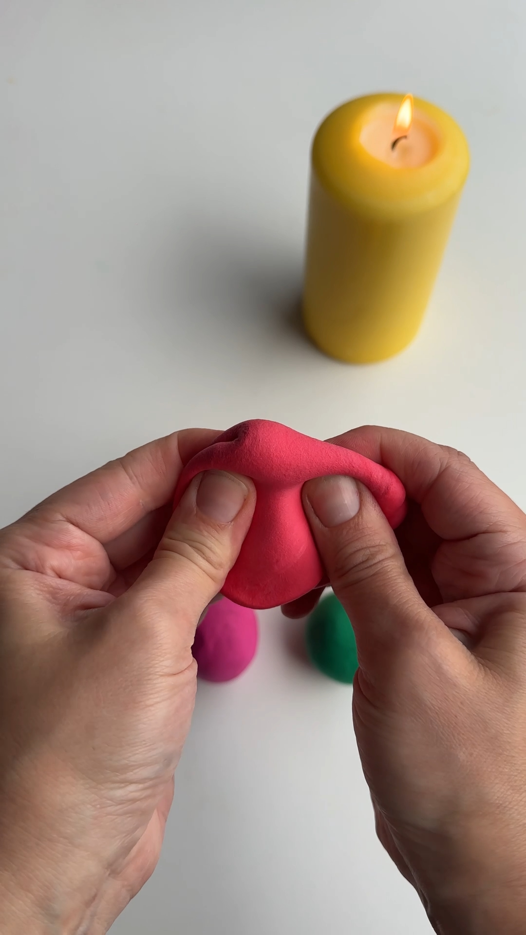 hands shaping pink foam clay into a small fruit shape