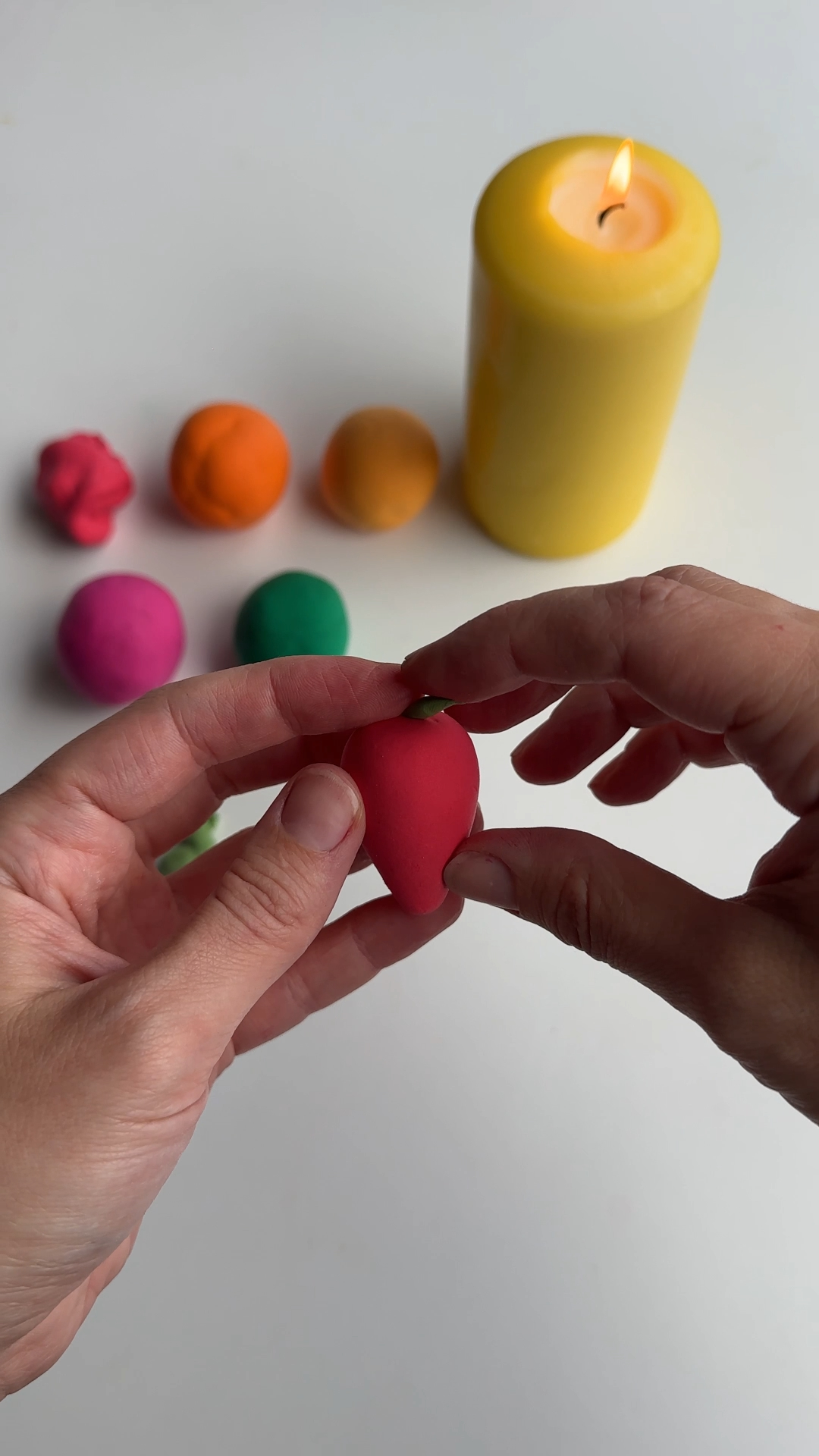 attaching a green clay leaf to the top of a strawberry shape