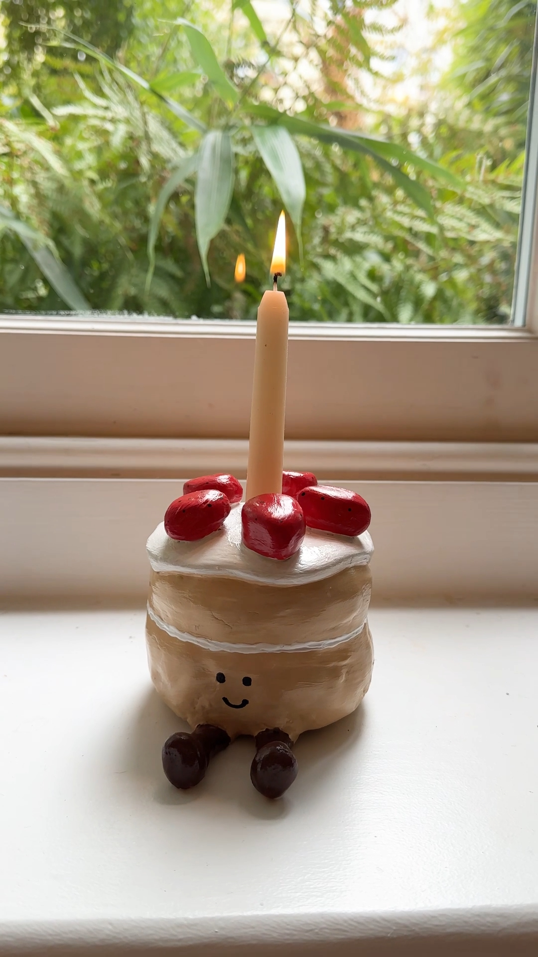 finished jellycat-inspired clay cake candle holder with strawberries, smiling face, and a lit tealight, on a windowsill