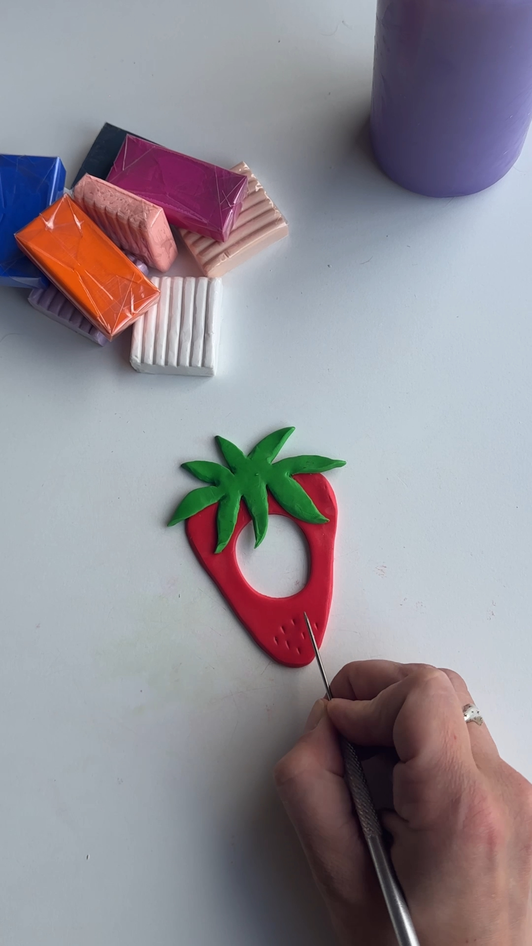 needle tool pressing seed details into a red polymer clay strawberry hair pin