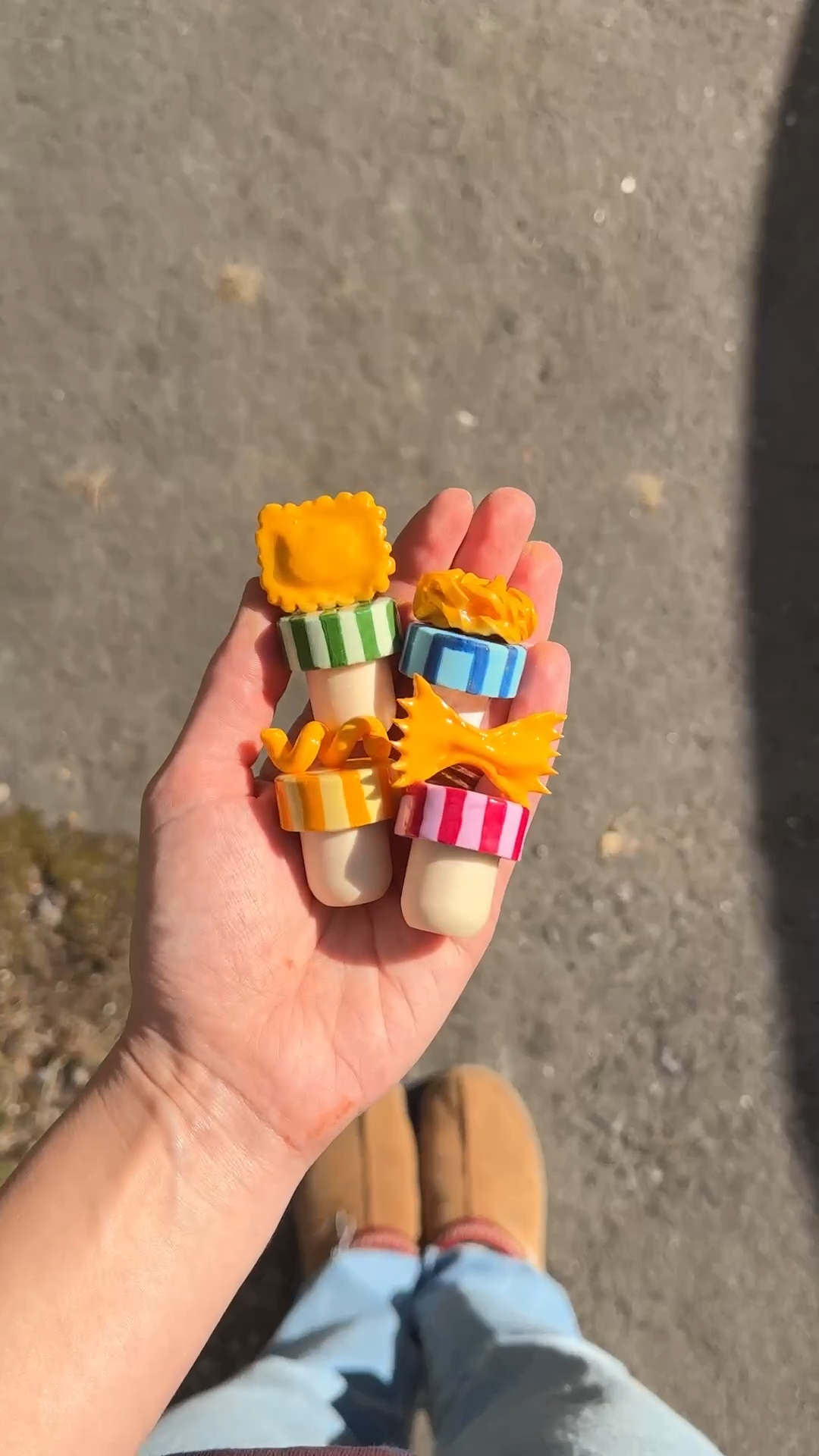 hand holding four finished diy pasta wine stoppers with colourful striped tops and polymer clay pasta — ravioli, pasta nest, fusilli, farfalle
