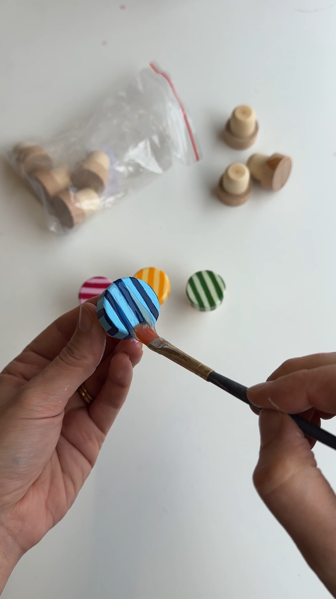 gloss varnish being brushed over colourful painted wine stopper tops to seal the stripes