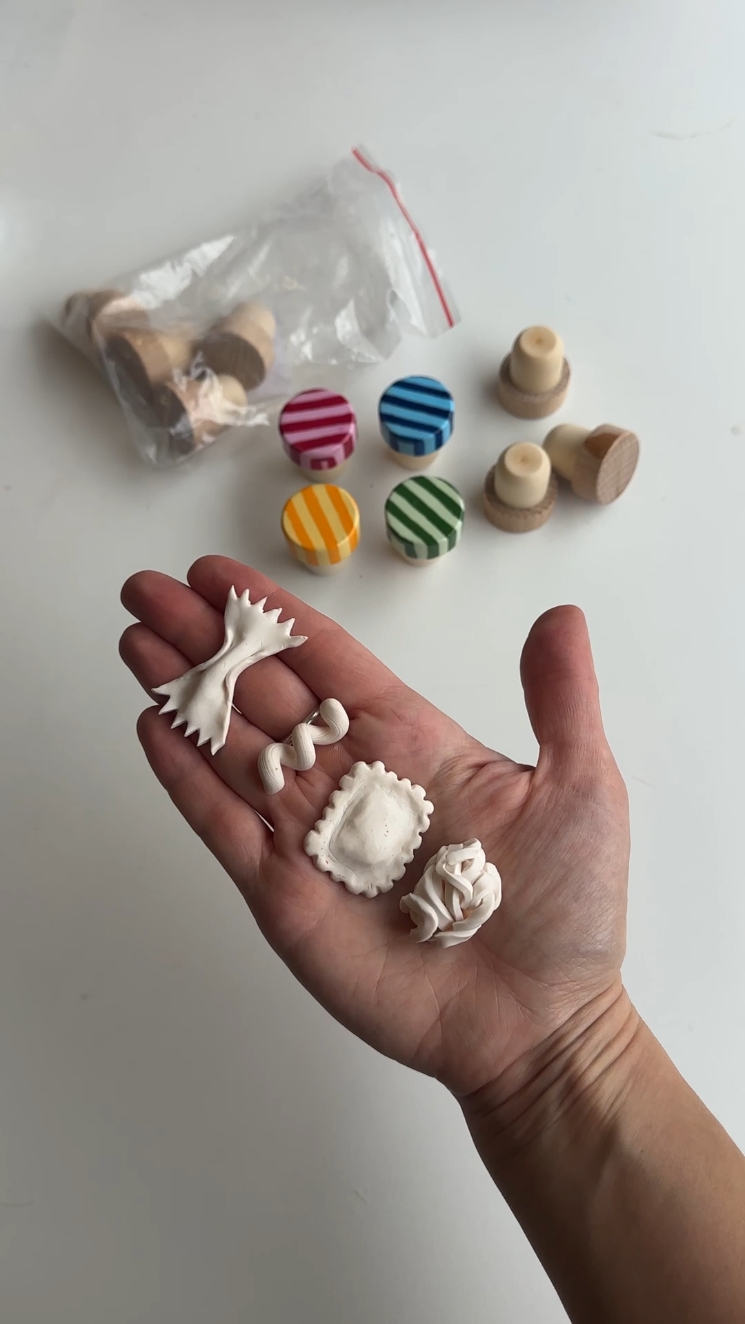 four baked polymer clay pasta shapes lined up on an outstretched hand