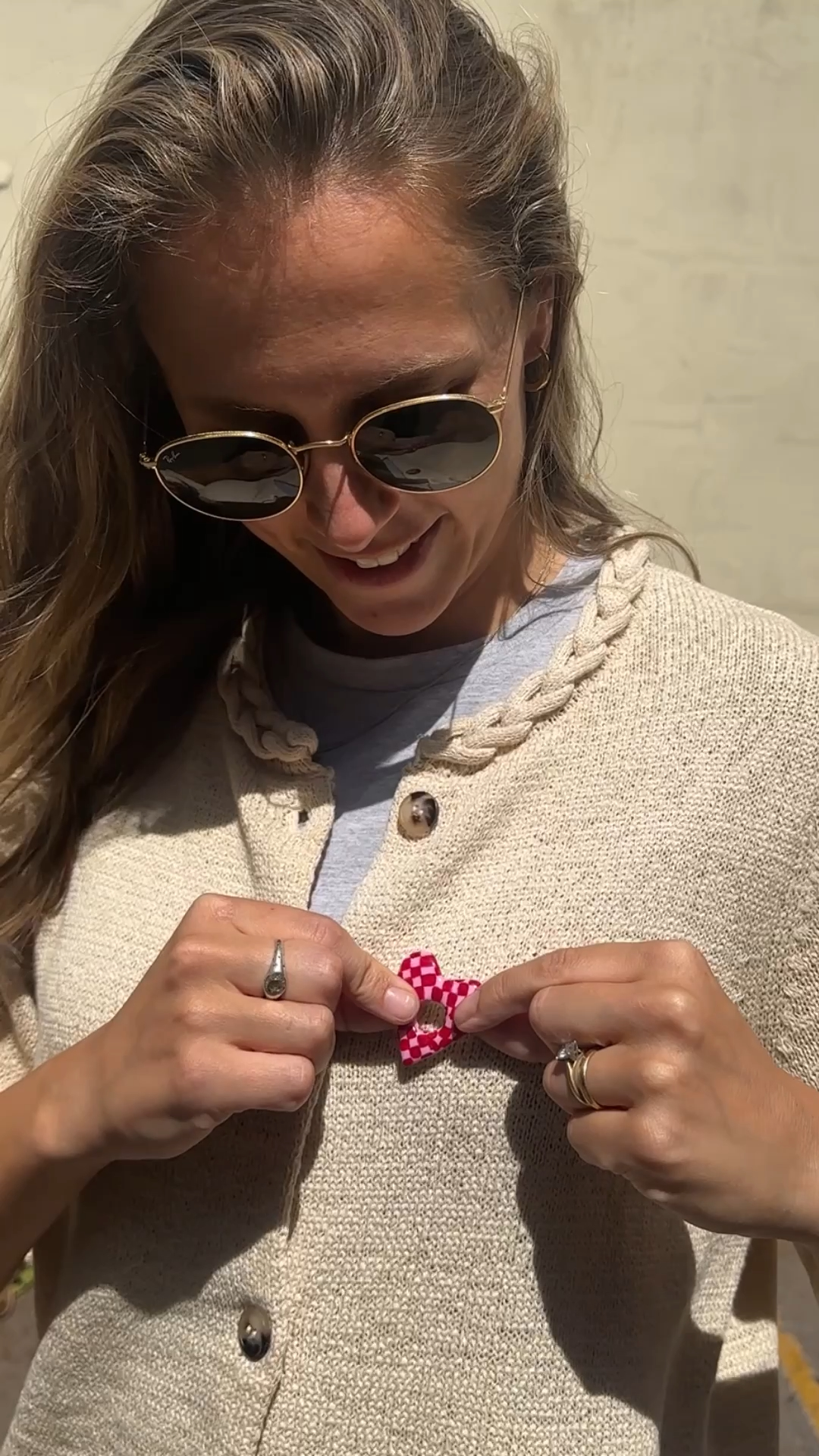 hands attaching a red and pink heart clay sunglasses holder worn on a knitted top