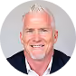 Smiling bald man with a white beard wearing a dark blazer and pink shirt.
