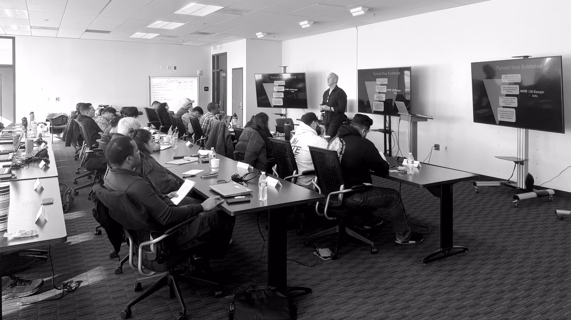 Group of people seated in a classroom attending a presentation with two large screens.