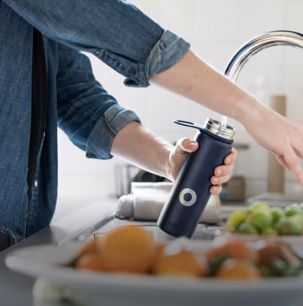 Person filling a reusable bottle from a kitchen tap