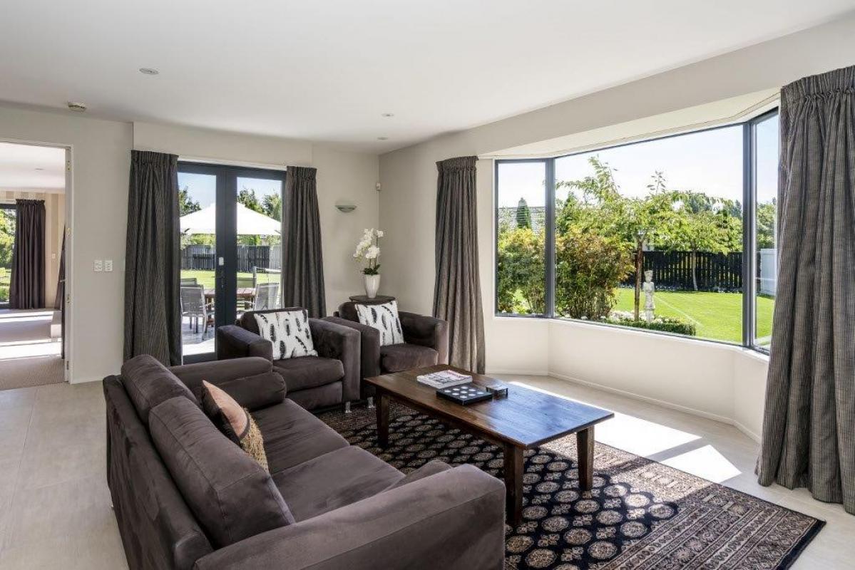 Open-plan living room with dark sofa, timber flooring, large sliding doors and views to the garden