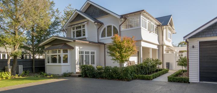 Evening exterior of the Kiteroa home with warm interior lighting visible through large windows and cedar cladding illuminated at dusk