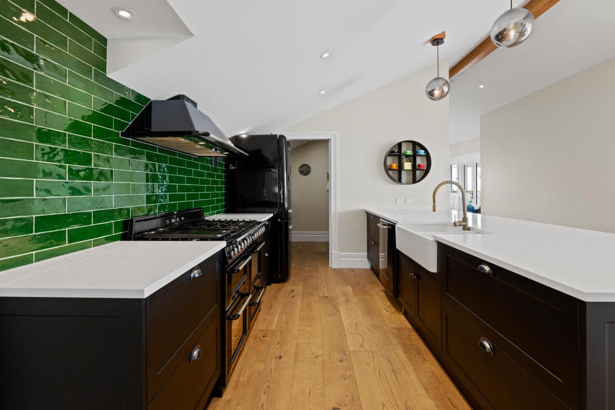 Modern kitchen with dark cabinetry, green splashback tiles, timber flooring and open shelving