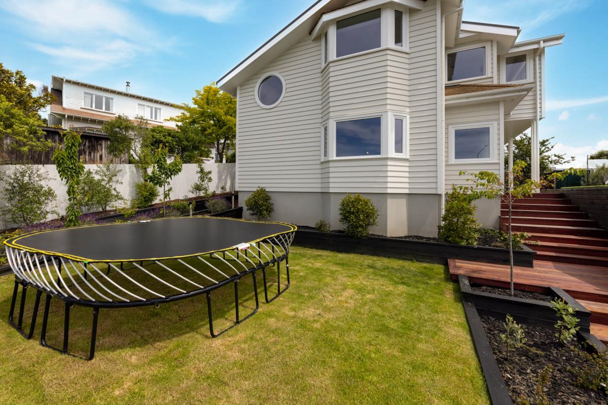 Side view of the Cashmere Hills home showing white weatherboard cladding, timber deck, landscaped garden and city views beyond