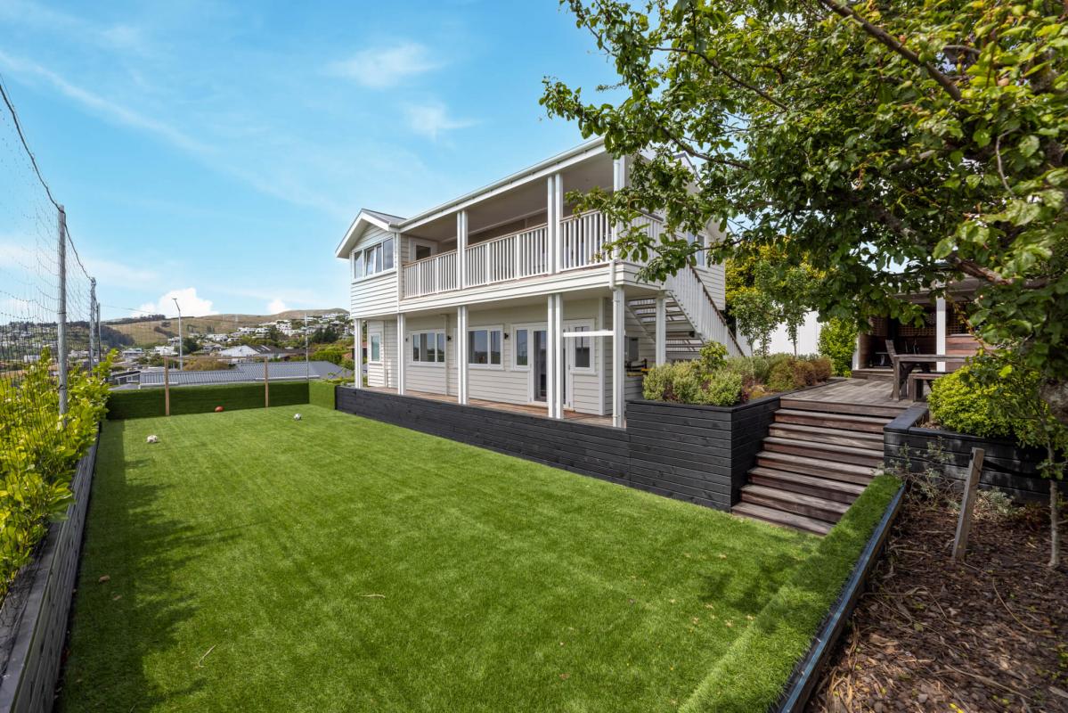 Side view of the Cashmere Hills home showing white weatherboard cladding, timber deck, landscaped garden and city views beyond