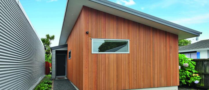 Exterior of a compact two-bedroom inner-city home in Christchurch Central featuring vertical cedar timber cladding, mono-pitch roofline and corrugated metal garage door