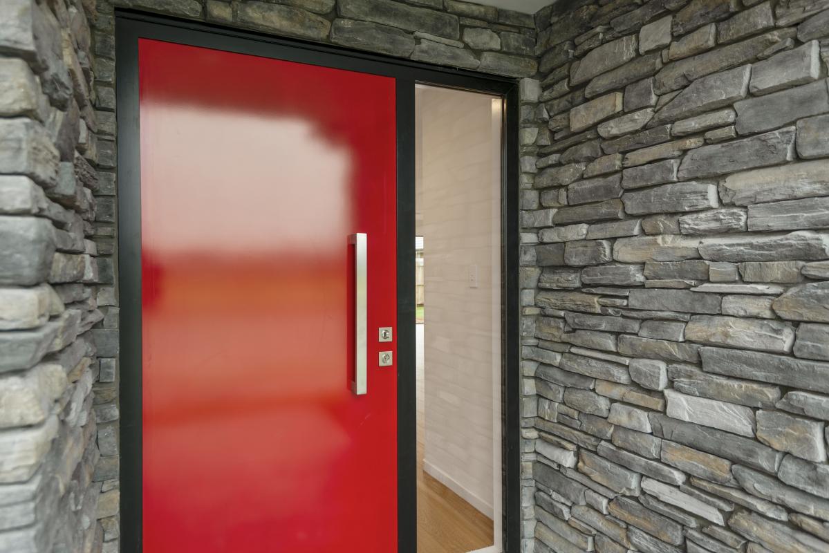 Close-up of red front door with schist stone feature wall and timber detail at the Halswell Haven home
