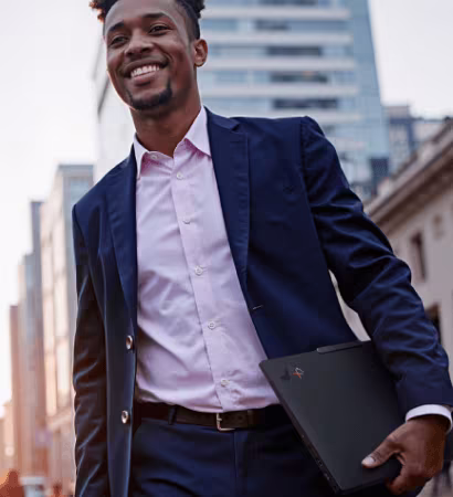 Business professional walking outdoors carrying Lenovo ThinkPad laptop in urban setting.