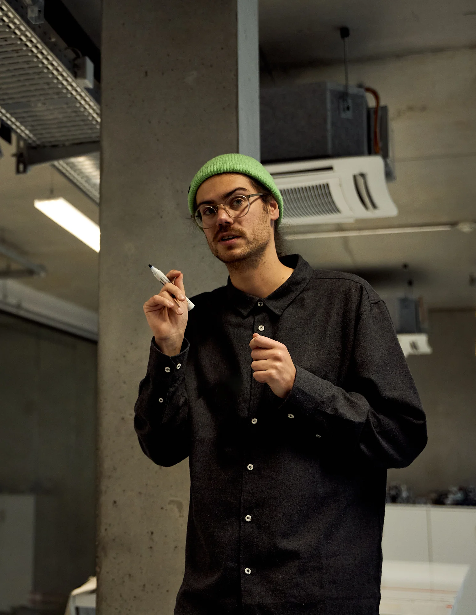 Torben Andresen wearing a green beanie and glasses, speaking and holding a white marker in an indoor office setting.