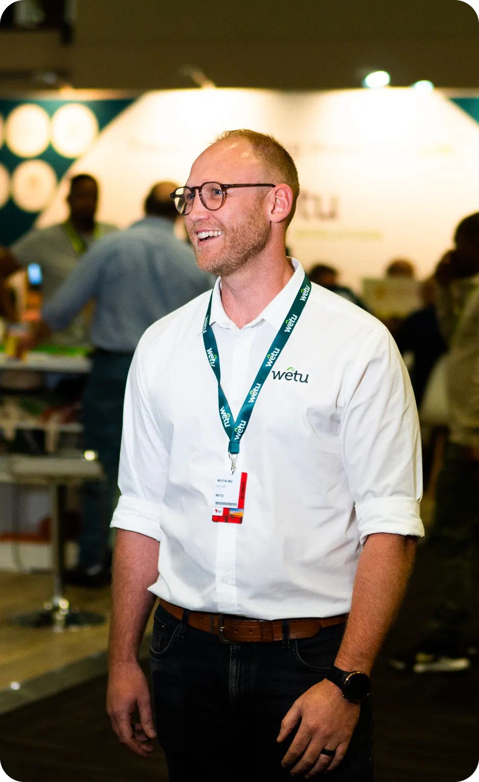 Smiling man wearing glasses and a white shirt with a Wetu logo and event badge on a lanyard.