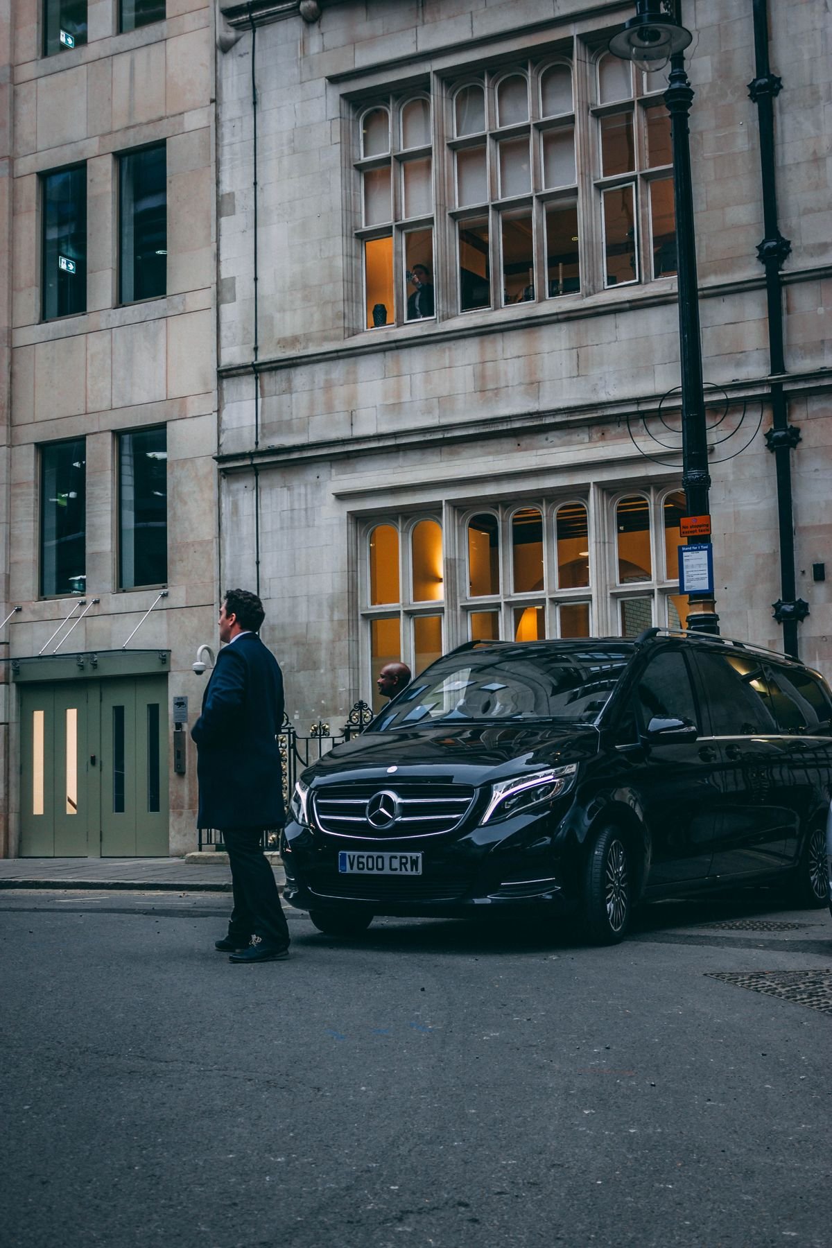 Professional chauffeur standing beside a Mercedes vehicle outside a city building
