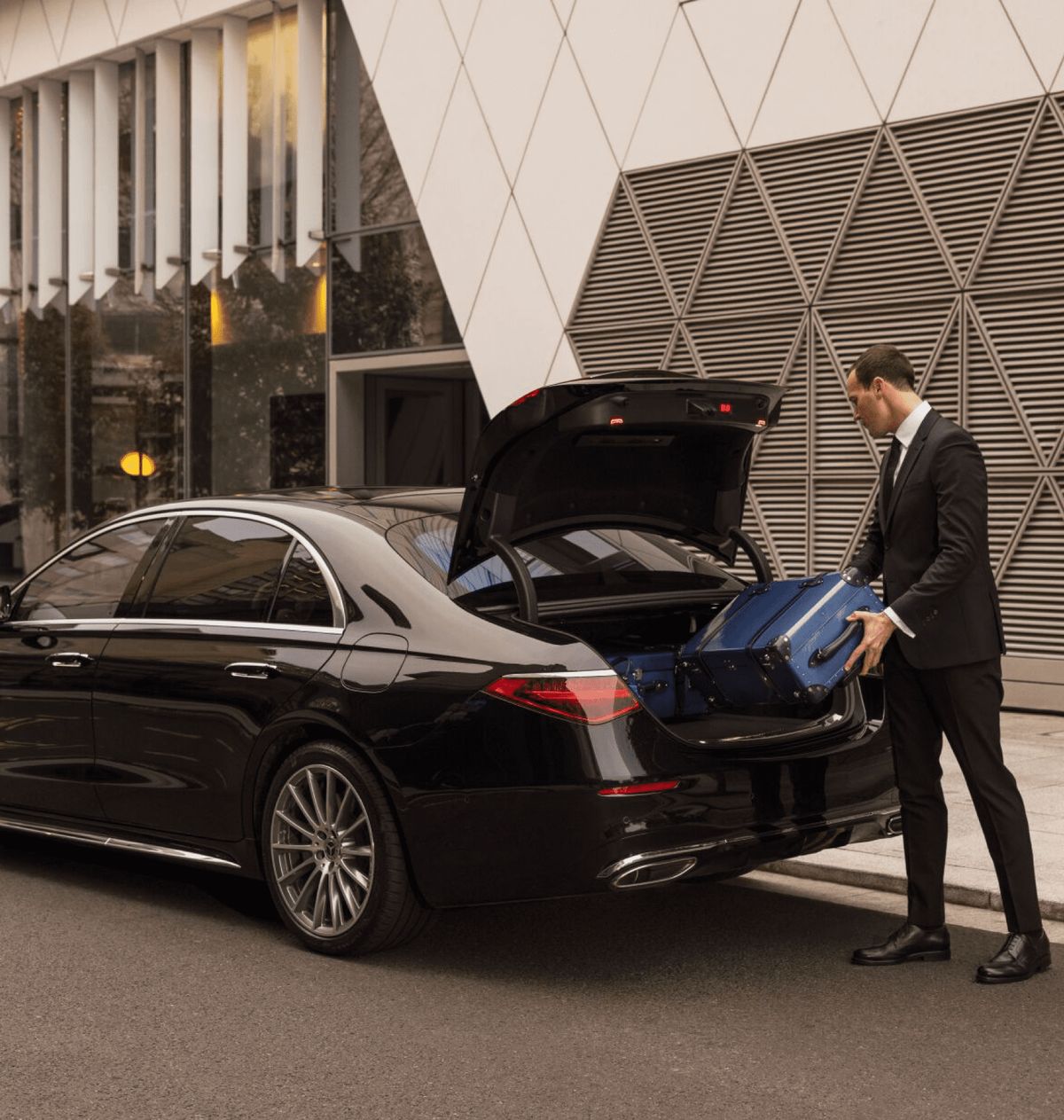 Chauffeur placing luggage into the boot of a black Mercedes saloon