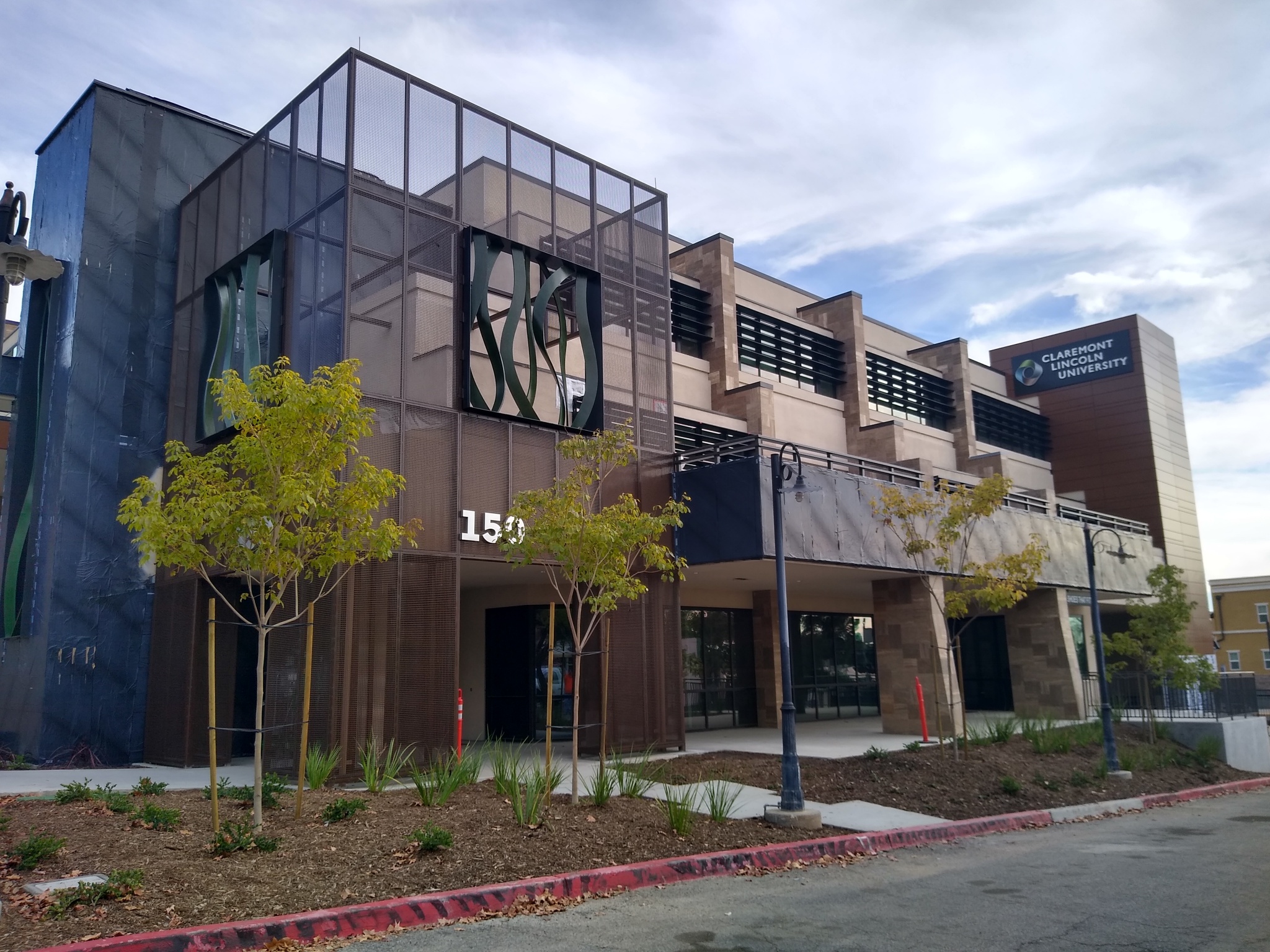 “Exterior view of Claremont Lincoln University building in California, featuring glass and metal façades, landscaped trees, and a sidewalk along the street.