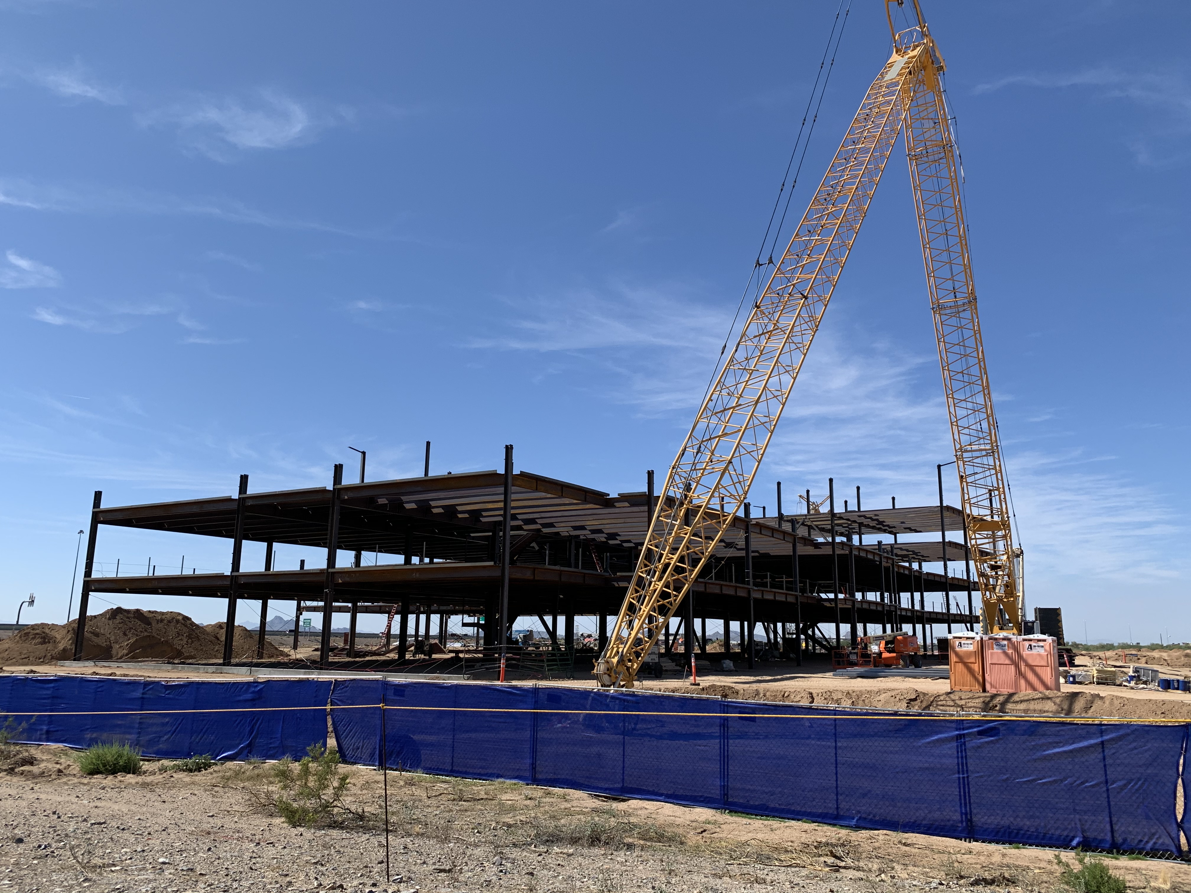 Steel frame of an office building under construction in Scottsdale, Arizona, with a large yellow crane lifting materials at the site under a clear blue sky