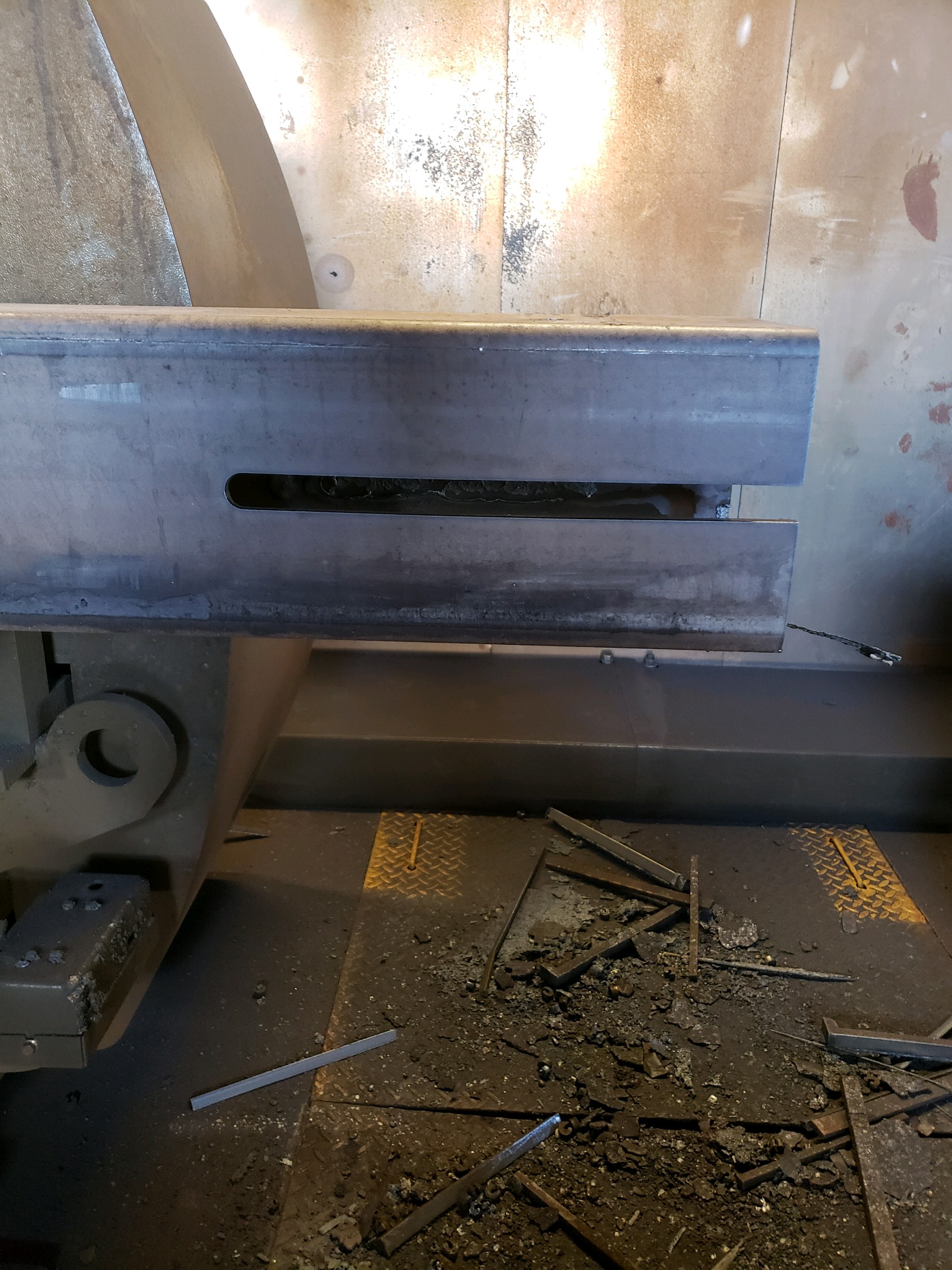 Close-up of a steel beam during processing, showing a precision-cut slot with metal shavings on the shop floor