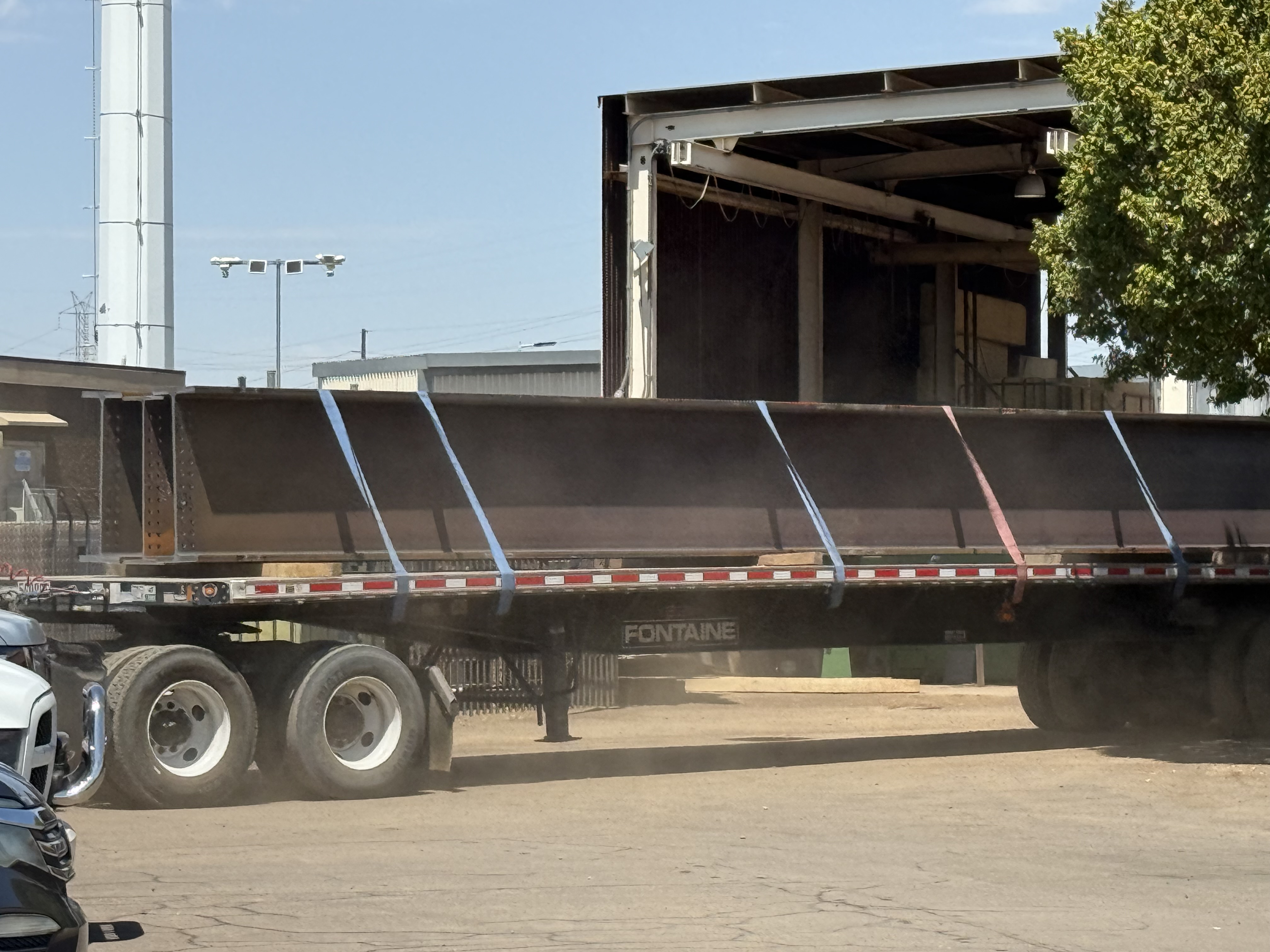 Processed steel beams secured with straps on a flatbed trailer, prepared for transport from a steel fabrication facility