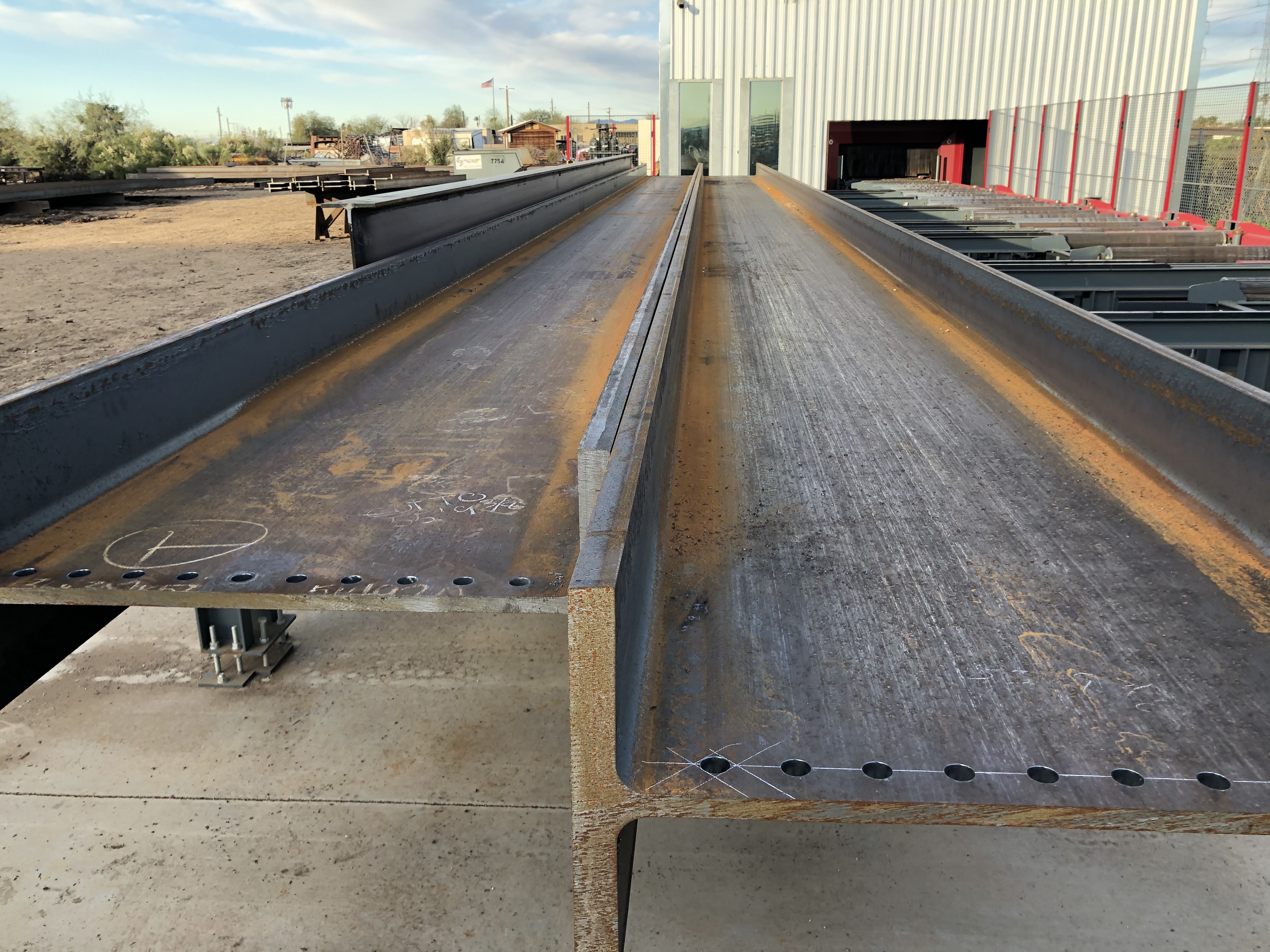Long steel beams with drilled bolt holes aligned in rows inside a steel fabrication facility