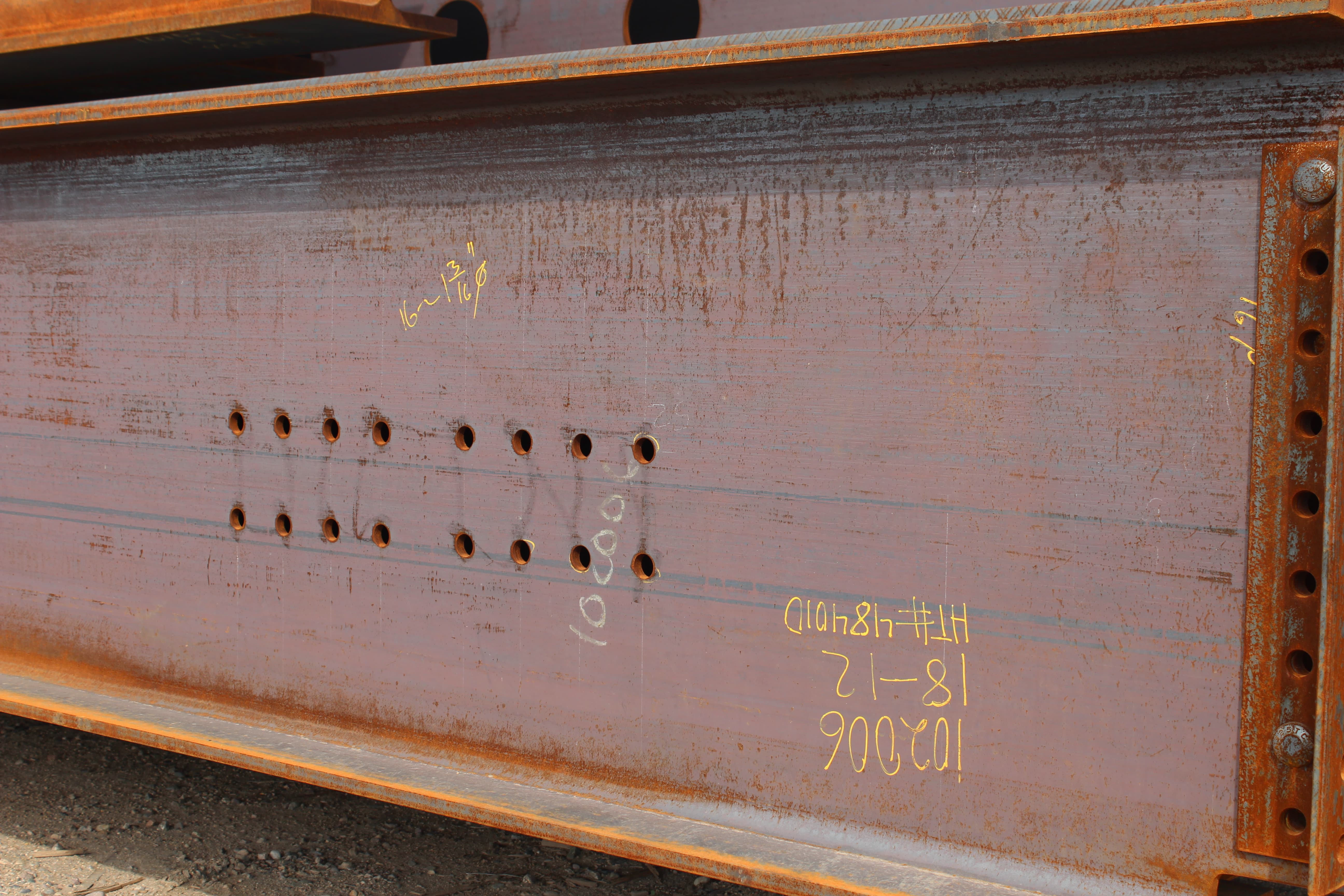 Structural steel beam with rows of drilled bolt holes and layout markings, prepared for fabrication and assembly
