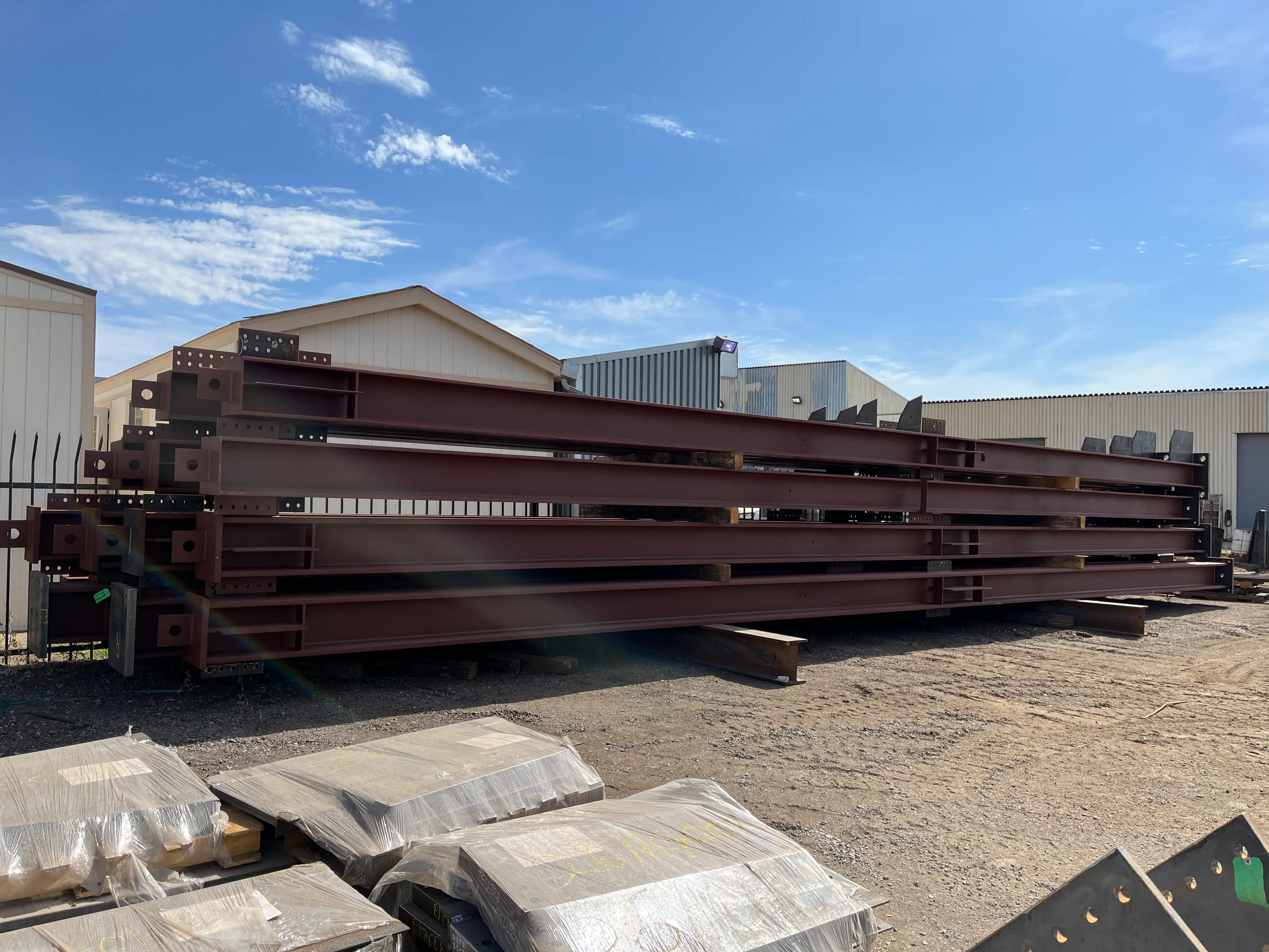 Fabricated structural steel beams stacked in a yard, showing bolted end plates and components ready for delivery