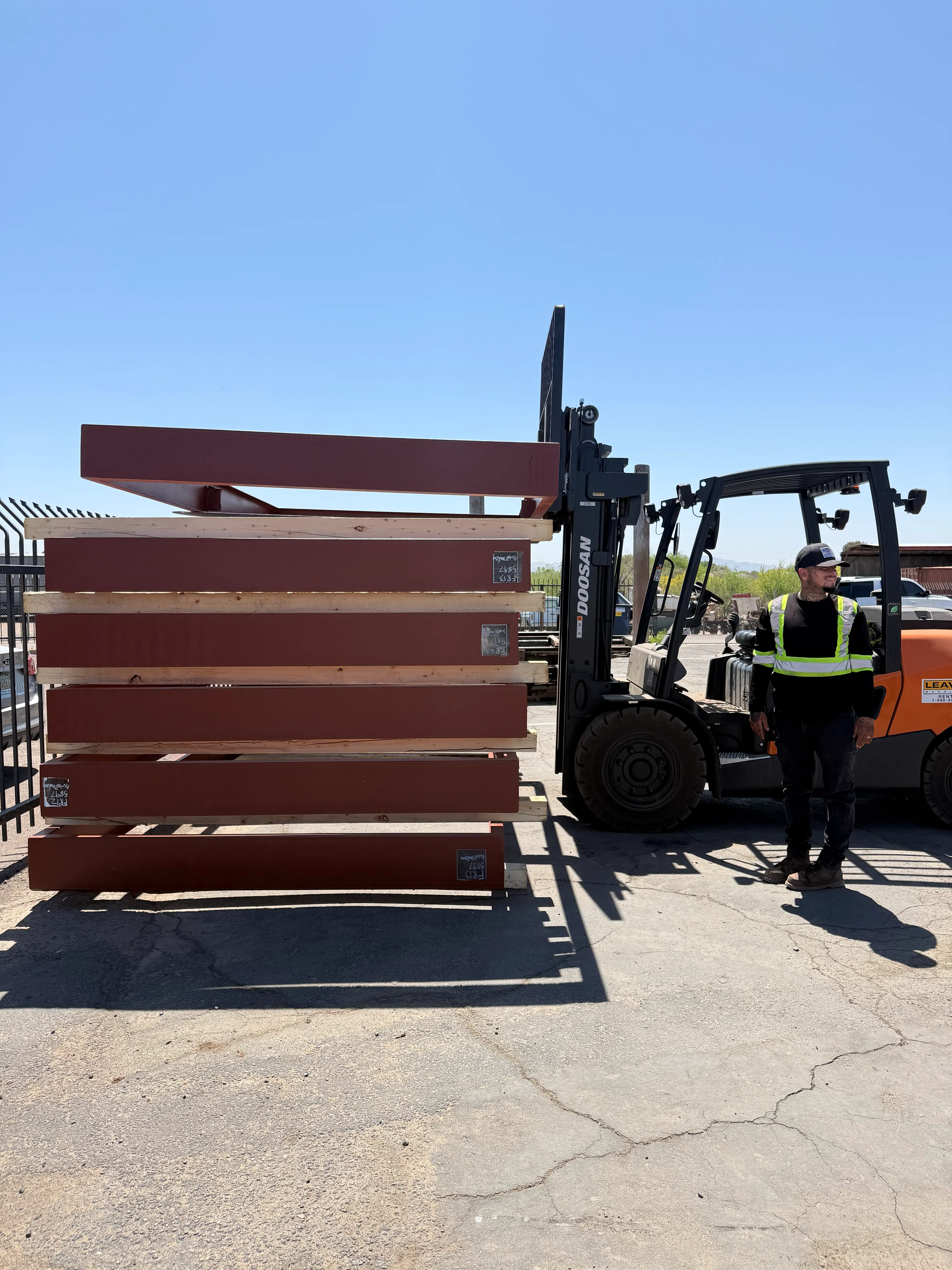 Stacked fabricated steel frames being handled by a forklift in a fabrication yard