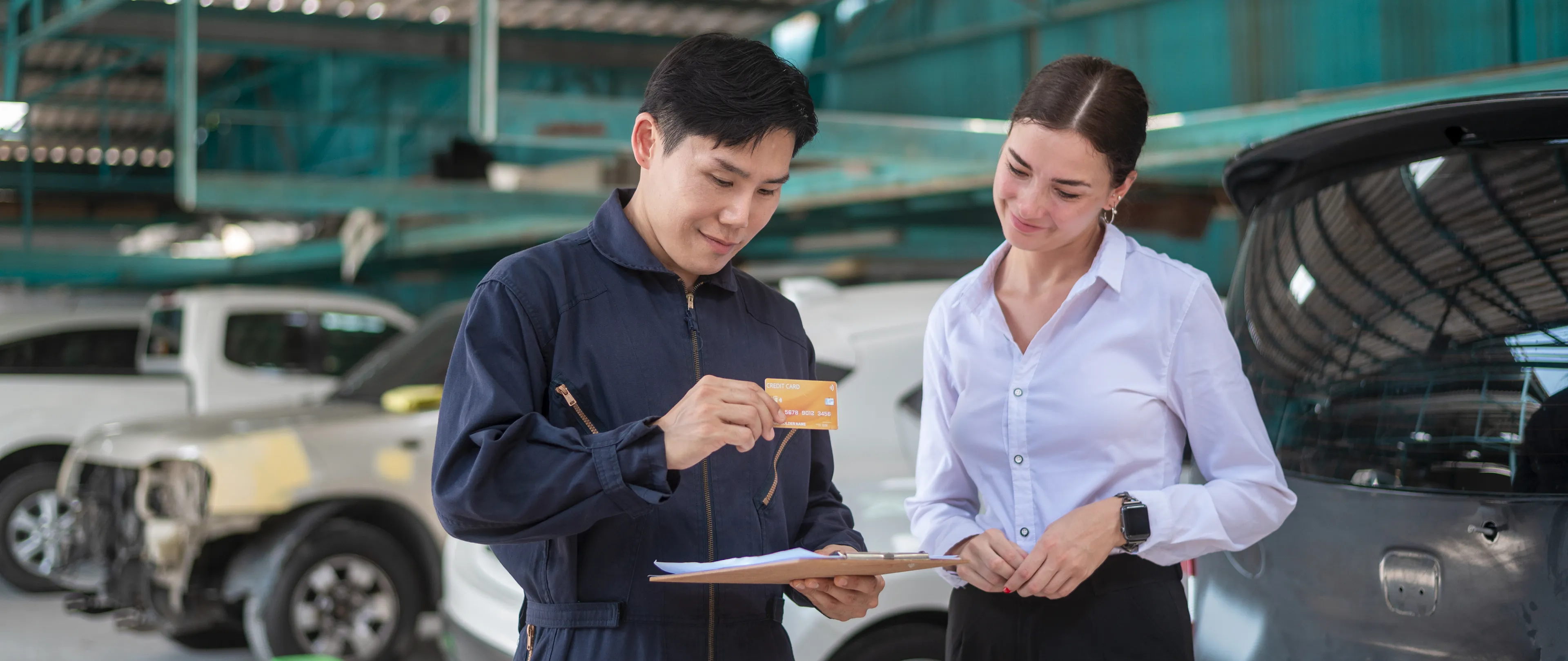 Image of car salesperson helping customer at a dealership in front of cars. 