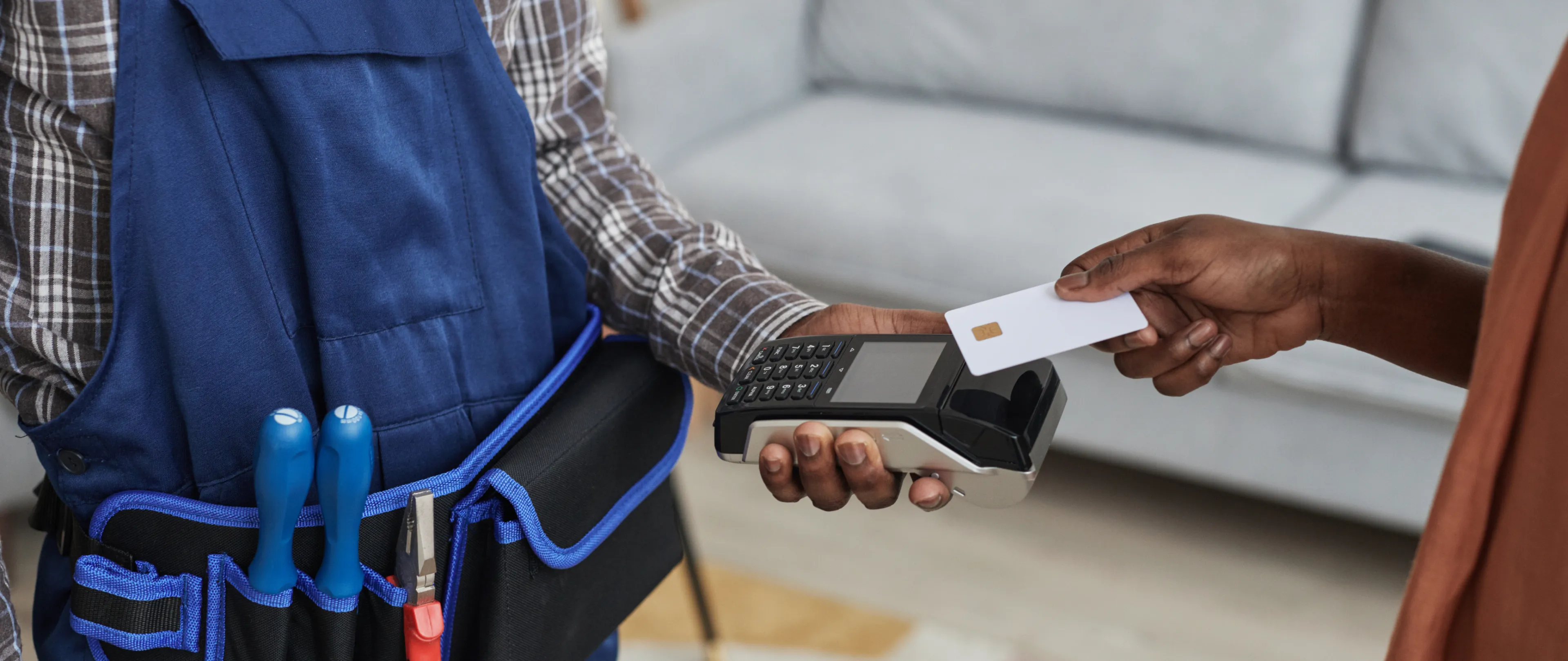 A field technician wearing a tool belt accepting a digital payment with a credit card on a mobile device.