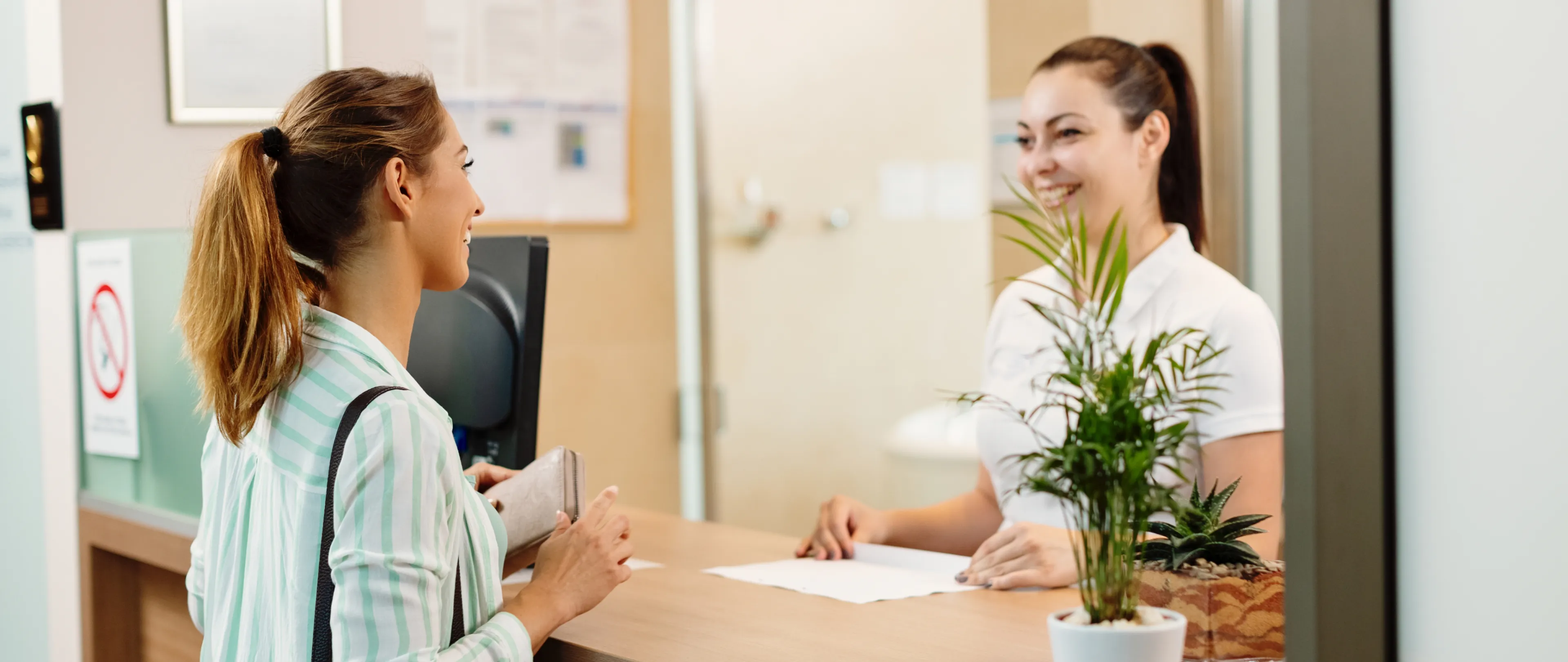 A healthcare employee consulting with a patient at a check-in desk.