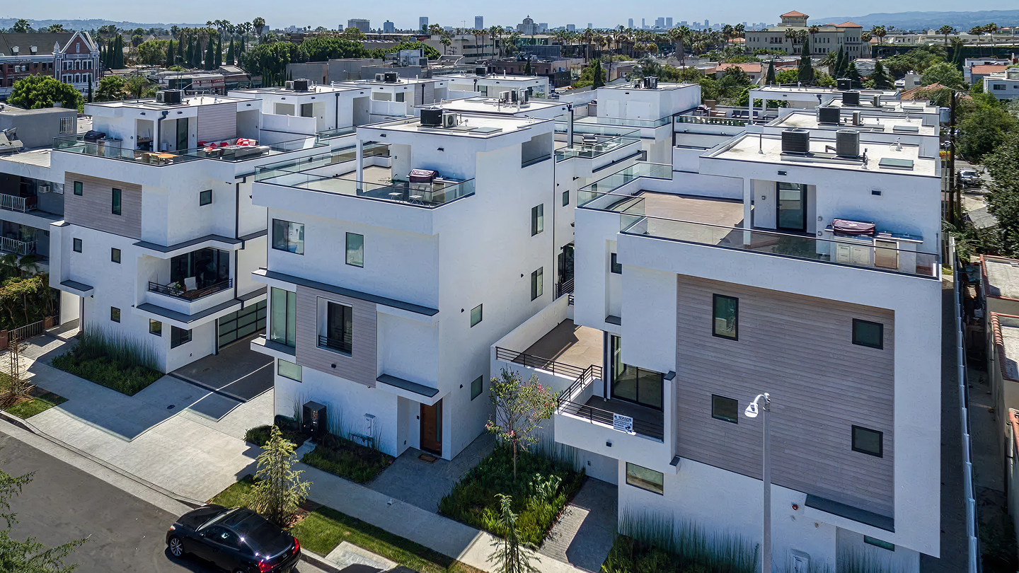 Modern white multi-story residential buildings with rooftop patios in an urban neighborhood.