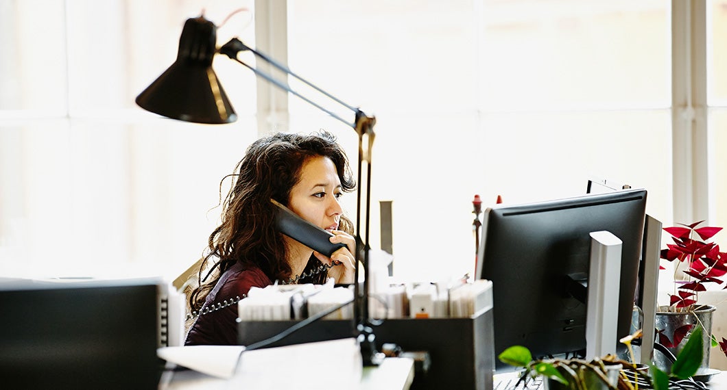 A businesswoman sitting at a workstation in an office on the phone