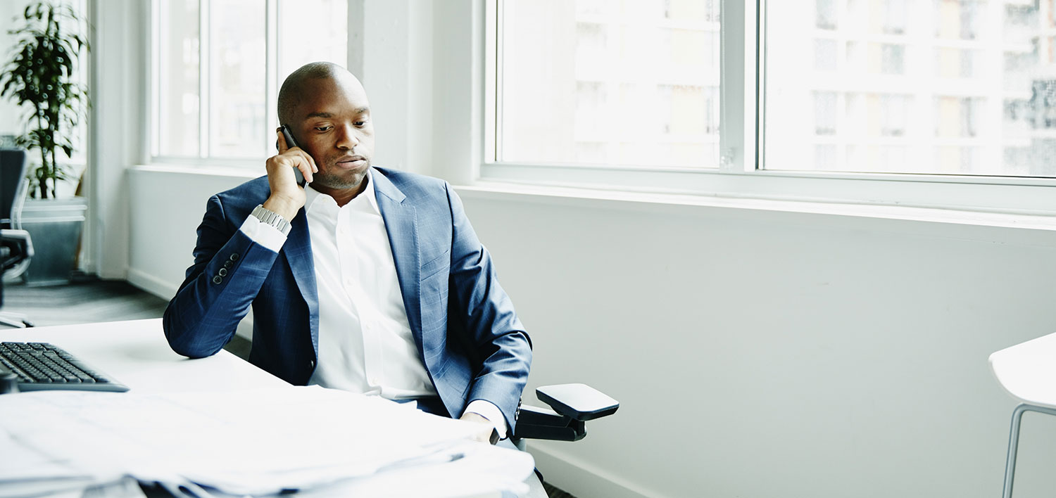 Frustrated man sitting at office workstation while on a smartphone