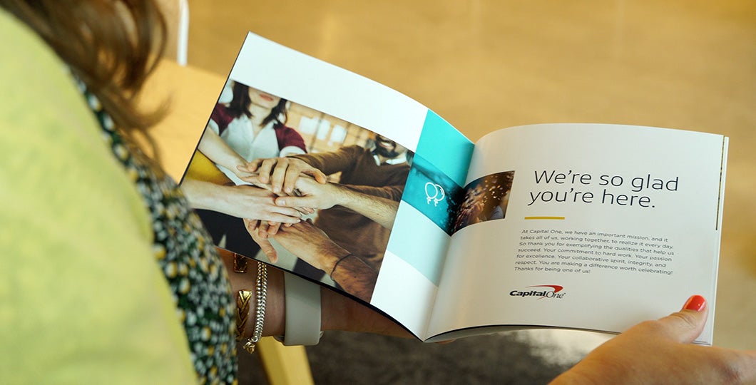Capital One employee holding a book from the company stating "We are so glad you're here."