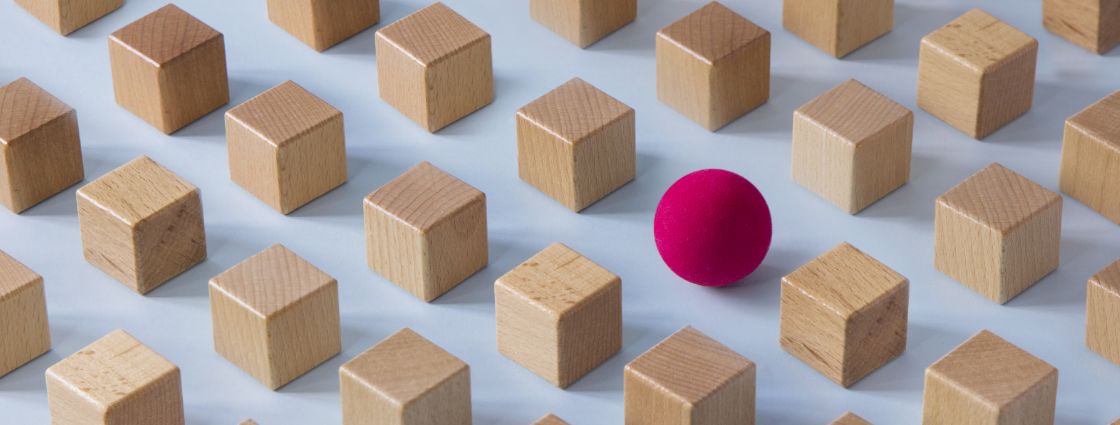 A single pink sphere surrounded by wooden cubes.