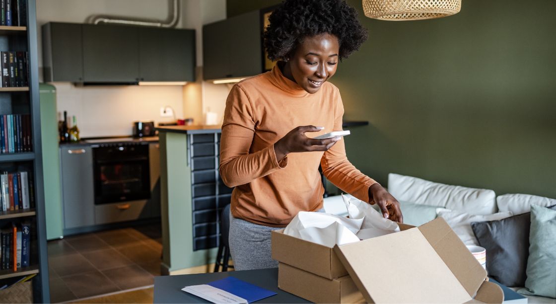 A virtual employee taking a photo of a box of company gifts in their home office.