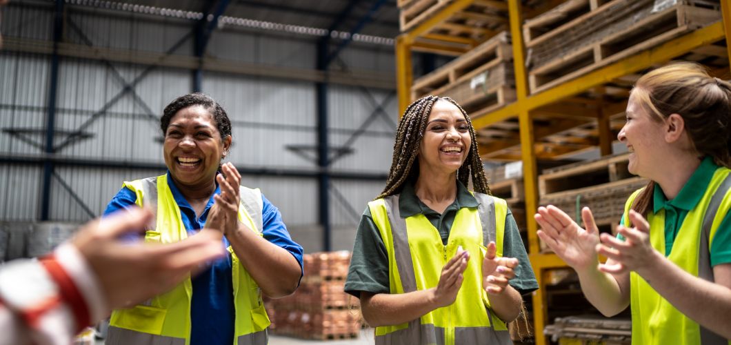 Offline manufacturing employees celebrate during a team huddle.