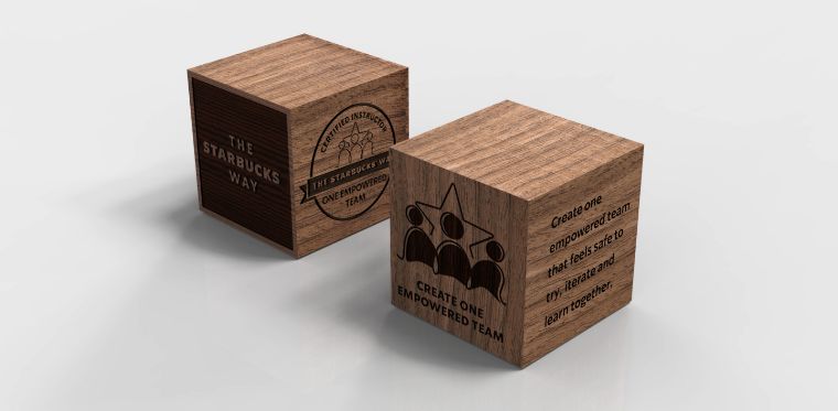 A cube-shaped custom award made of wood with a company logo, value statement, and employee recognition award name on each side