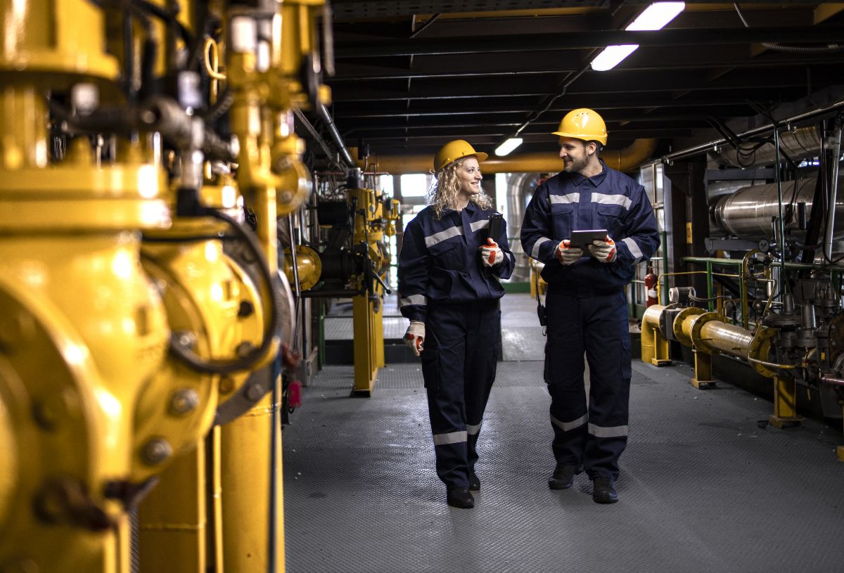 Factory workers in safety equipment walking by gas pipes