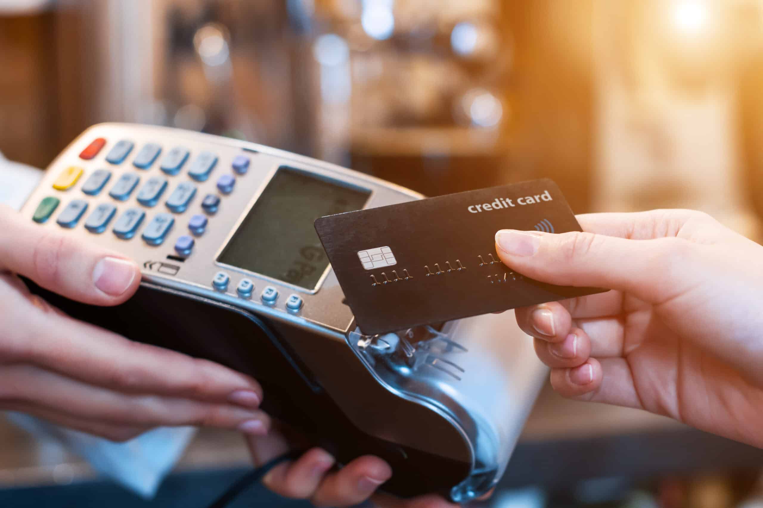 Person holding a black credit card near a payment terminal for a contactless transaction.